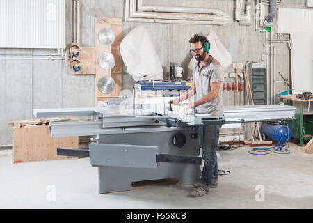 Full length of carpenter using a sliding table saw in workshop Stock Photo