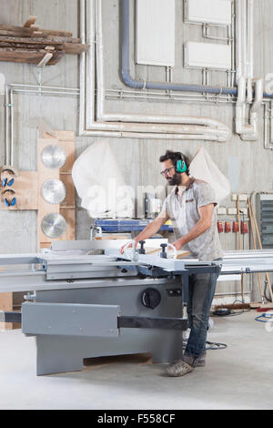 Full length of male carpenter using a sliding table saw in workshop Stock Photo