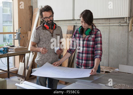 Male and female carpenters with blueprint in workshop Stock Photo