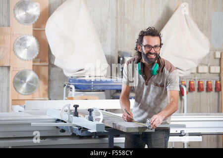 Portrait of happy male carpenter measuring lumber in workshop Stock Photo