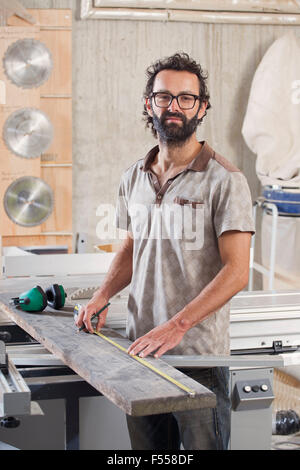 Portrait of male carpenter measuring wood in workshop Stock Photo