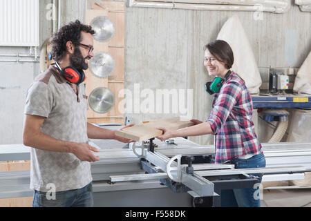 Carpenters laughing while using sliding table saw in workshop Stock Photo