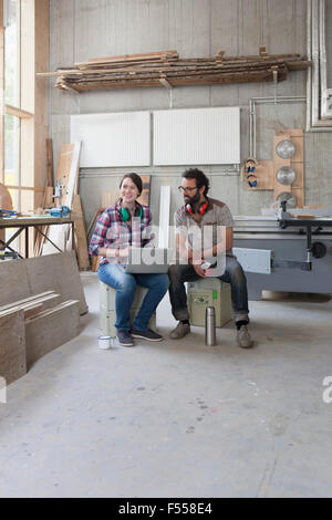 Full length of happy carpenters using laptop in workshop Stock Photo