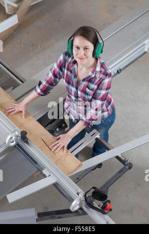 High angle portrait of happy female carpenter using a sliding table saw in workshop Stock Photo