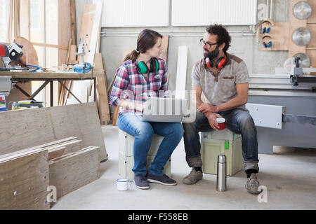 Full length of mid adult carpenters discussing while using laptop in workshop Stock Photo