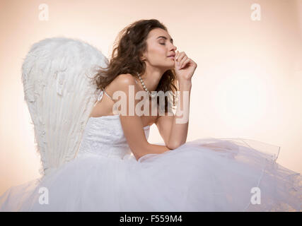 Bride with eyes closed wearing angel wings while sitting against colored background Stock Photo