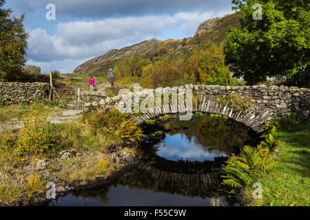 Two Walkers Just About to Cross the Packhorse Bridge over Watendlath Beck Stock Photo