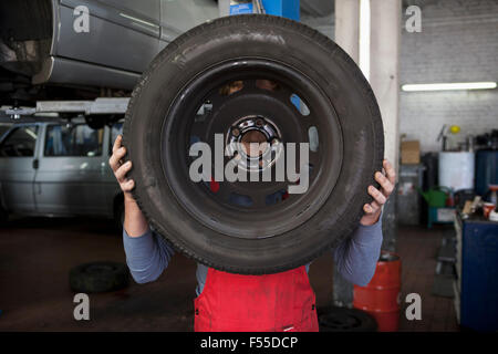 Mechanic holding tire in front of face at garage Stock Photo