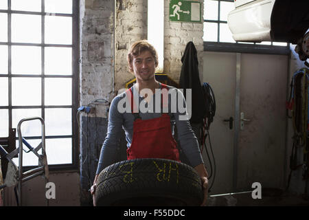 Portrait of smiling mechanic holding tire at garage Stock Photo