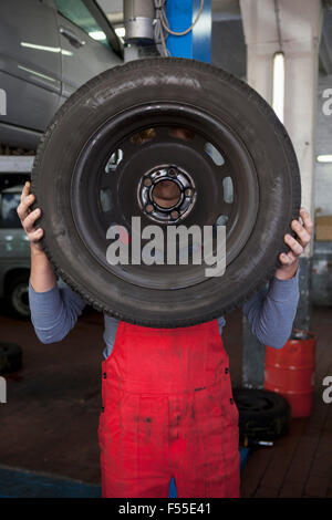 Mechanic holding tire in front of face at workshop Stock Photo