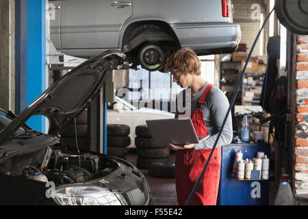 Mechanic using laptop while examining car engine at garage Stock Photo