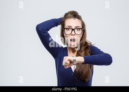 Portrait of shocked young woman holding hand with wrist watch and looking at camera isolated on a white background Stock Photo