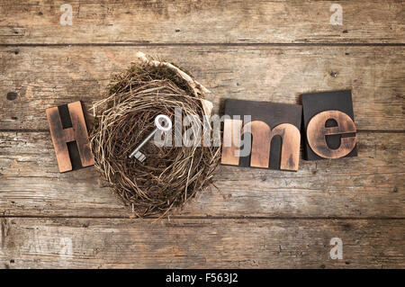 Home concept -word Home written with vintage letterpress printing blocks and bird nest containing a door key on rustic wood Stock Photo