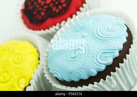 Three cupcakes on the white background. Yellow, blue and red with handmade decoration Stock Photo