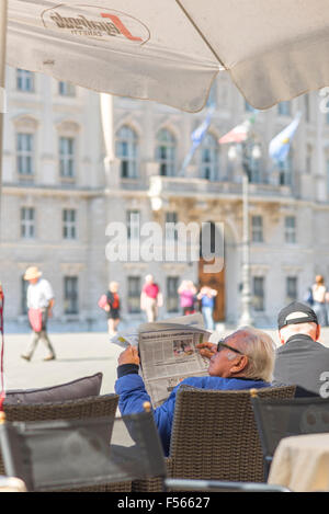 Man reading newspaper cafe, view of a senior male tourist relaxing outside a cafe in the Piazza dell'Unita d'Italia, Trieste, Italy. Stock Photo