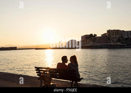 A young couple relax on the foreshore of the Venetian Harbour in Chania on the Island of Crete in Greece Stock Photo