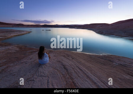 One woman sitting by the lake Powell clear evening sky and calm water Stock Photo