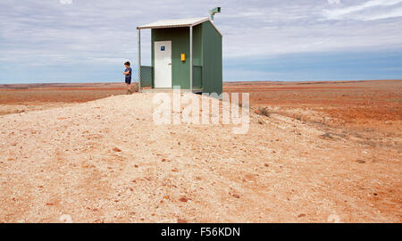 Humourous view of young boy beside isolated public toilet on vast barren red outback plains in remote area of Australia Stock Photo