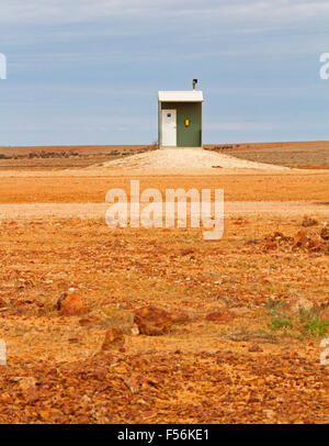 Humourous view of isolated public toilet on vast barren red stony outback plains in remote area of Australia under blue sky Stock Photo