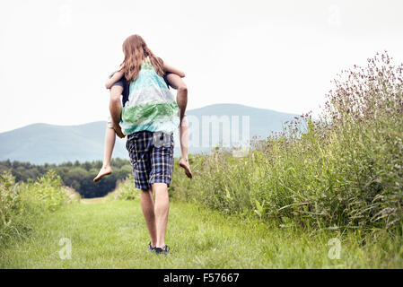 A man giving a young child a piggyback in a meadow. Stock Photo