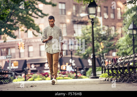 A man walking through a town square looking at his smart phone Stock Photo