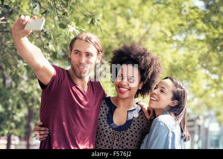 Three people, a man and two women, taking selfies in a city park Stock Photo