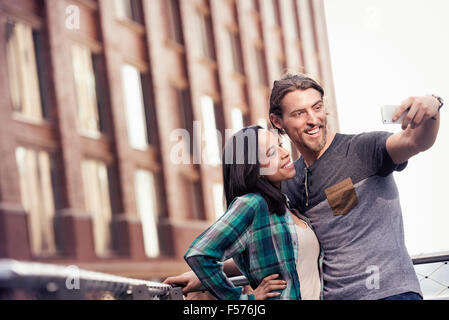 A couple, man and woman taking a selfie by a large building in the city Stock Photo