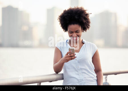 A woman leaning on a waterfront rail checking her cell phone Stock Photo