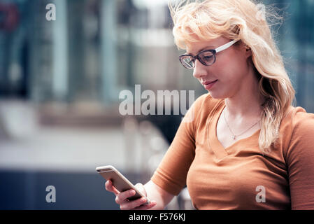 A blond woman on a street using her cell phone, checking for messages Stock Photo