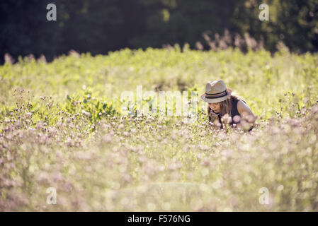 A child, a young girl in straw hat in a meadow of wild flowers in summer. Stock Photo