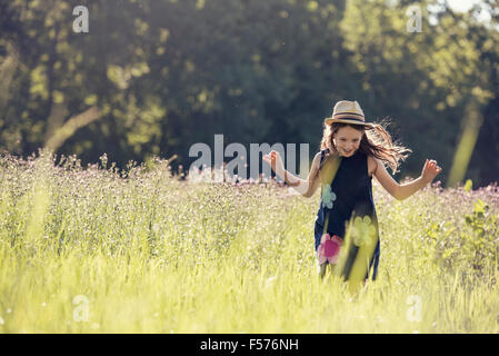 A child, a young girl in straw hat in a meadow of wild flowers in summer.