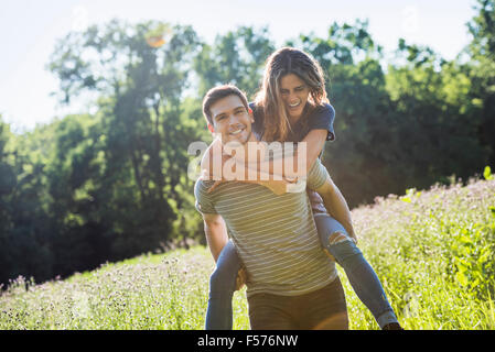 A couple, a man giving a young woman a piggyback, walking through a flower meadow in summer. Stock Photo