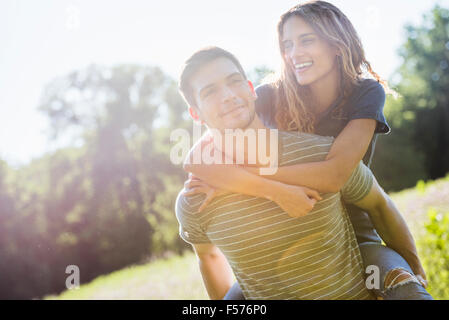 A couple, a man giving a young woman a piggyback, walking through a flower meadow in summer. Stock Photo