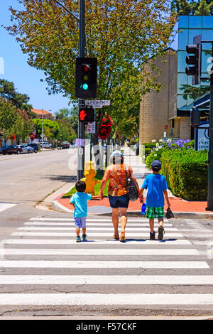 A mother holds the hands of her two children as she crosses a road on the pedestrian walkway in downtown Santa Paula CA Stock Photo