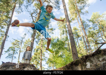 nine year old boy doing star jumps off a bank with his three years old sister watching in woodland, Sussex. UK. October. Stock Photo