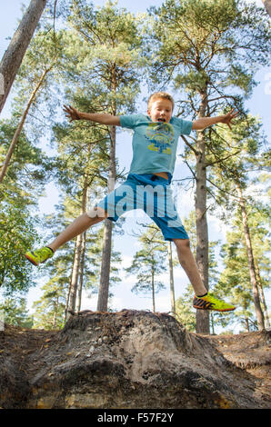 nine year old boy doing star jumps off a bank in woodland, Sussex. UK. October. Stock Photo