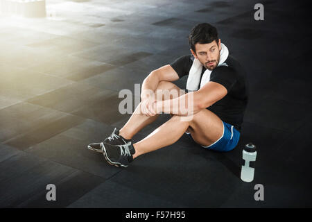 Sportsman wearing blue shorts and black t-shirt sitting on the floor in gym Stock Photo