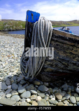 Prow of old wooden fishing boat on shingle beach with coil of rope Stock Photo