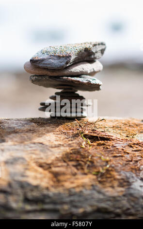 Thin pebbles carefully balanced on drifted log showing texture and depth of colour in the style of artist Andy Gray Stock Photo