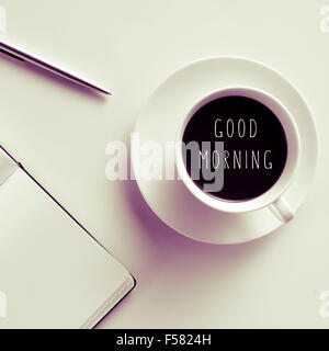 high-angle shot of a white table with a pen, a notebook, and a cup of coffee with the text good morning written in it Stock Photo