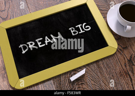 Dream Big - Yellow Chalkboard with Hand Drawn Text and White Cup of Coffee on Wooden Table.  Inspirational Quote. Top View. Stock Photo