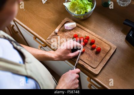 man cooking salad in the kitchen, male hands cutting tomatoes, healthy food Stock Photo