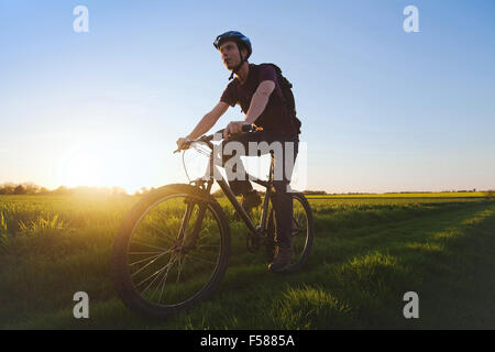 young sportive man riding bicycle outdoors at sunset Stock Photo