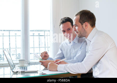 two smiling happy business men working on project in the office Stock Photo