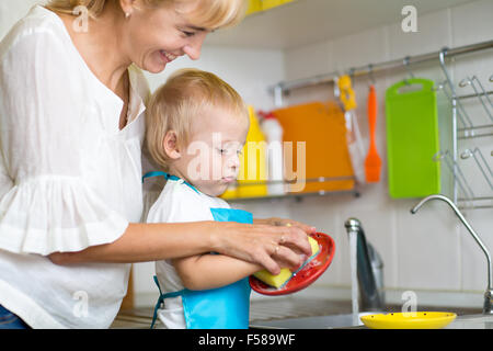 Kid boy and mother washing dishes - having fun together in the kitchen Stock Photo