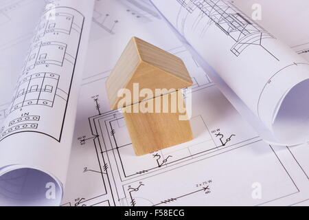House shape made of wooden blocks and rolls of diagrams lying on electrical construction drawings of house, concept of building Stock Photo