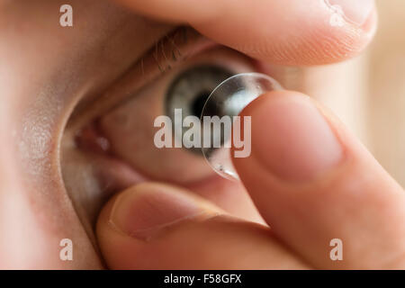 A man is inserting a contact lens into his left eye. Stock Photo