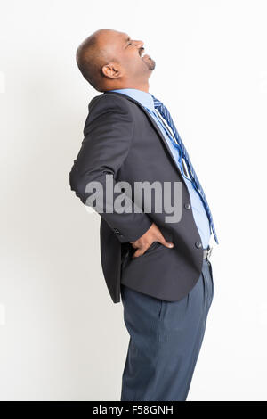 Indian businessman backache, holding his spine with painful face expression, standing on plain background. Stock Photo