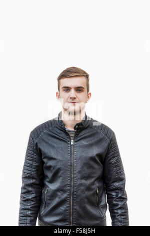 Medium shot of a young man wearing a leather jacket standing behind a white wall. Stock Photo