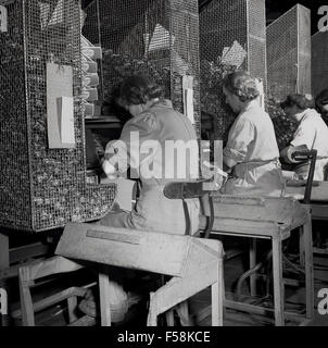 1950s historical picture of female factory workers at the Ever Ready battery factory putting cases held in large cages onto batteries. Stock Photo